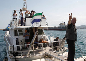 Um dos participantes na flotilha saúda de bordo do “Juliano” à partida de Perama, perto de Atenas